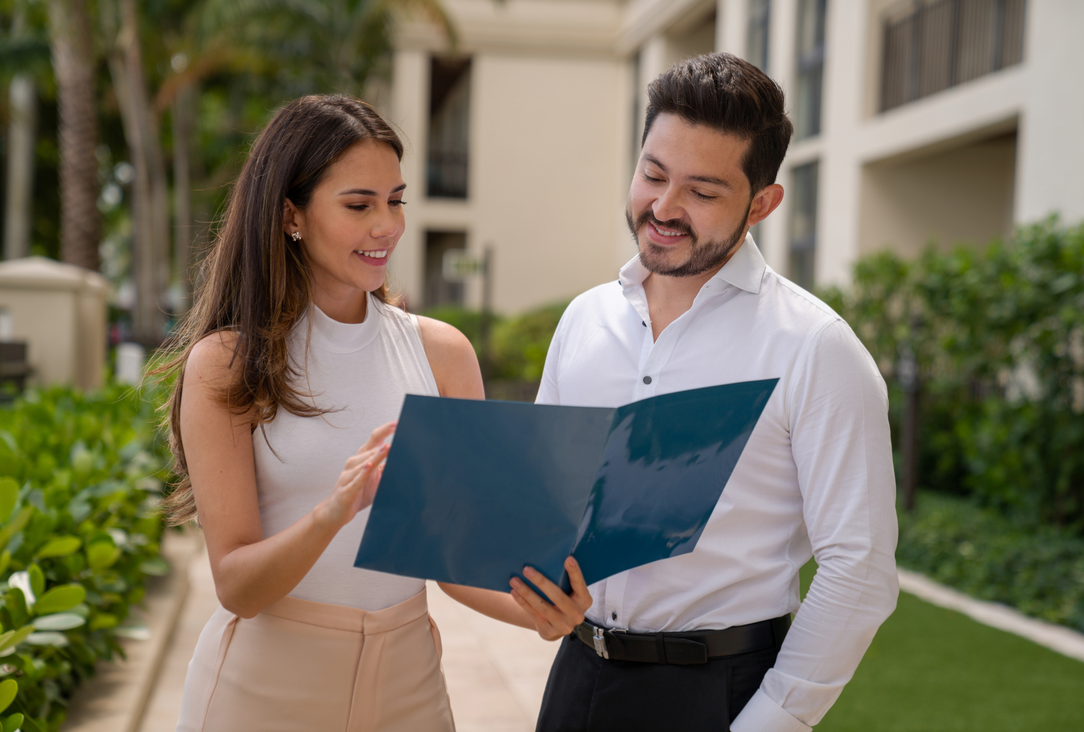 Real Estate Agent showing a contract to her client outside a property for sale - home ownership concepts